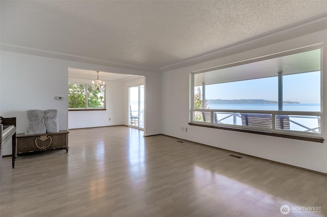 unfurnished living room with a chandelier, a textured ceiling, wood finished floors, baseboards, and a water view