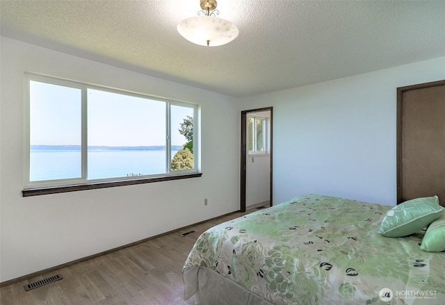 bedroom with a textured ceiling, wood finished floors, baseboards, and a water view