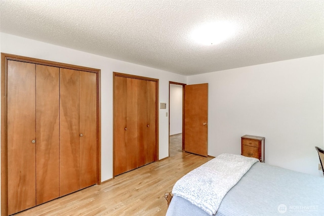 bedroom featuring multiple closets, light wood-style flooring, and a textured ceiling