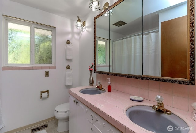 full bathroom with healthy amount of natural light, toilet, decorative backsplash, and double vanity