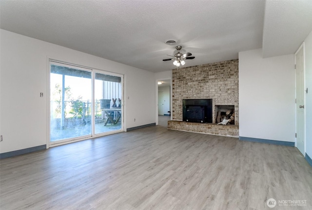 unfurnished living room featuring a ceiling fan, light wood-style floors, baseboards, a fireplace, and a textured ceiling