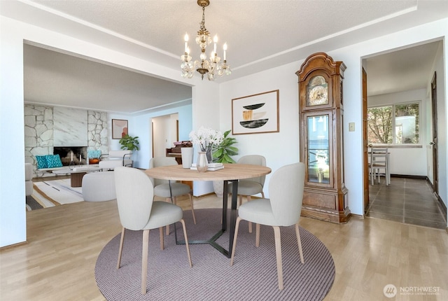dining area with a chandelier, light wood-style floors, a fireplace, and a tray ceiling