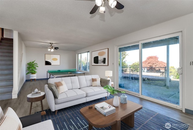 living area with a ceiling fan, a textured ceiling, wood finished floors, and stairway