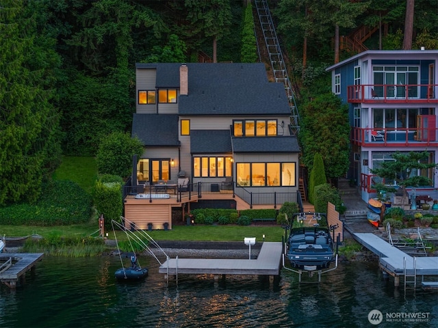 back of house featuring boat lift, a water view, and a shingled roof