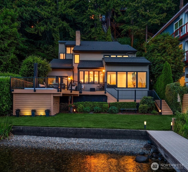 rear view of house with a chimney, a wooden deck, a lawn, roof with shingles, and stairs