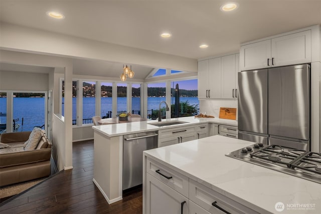 kitchen with a sink, a peninsula, stainless steel appliances, white cabinets, and dark wood-style floors