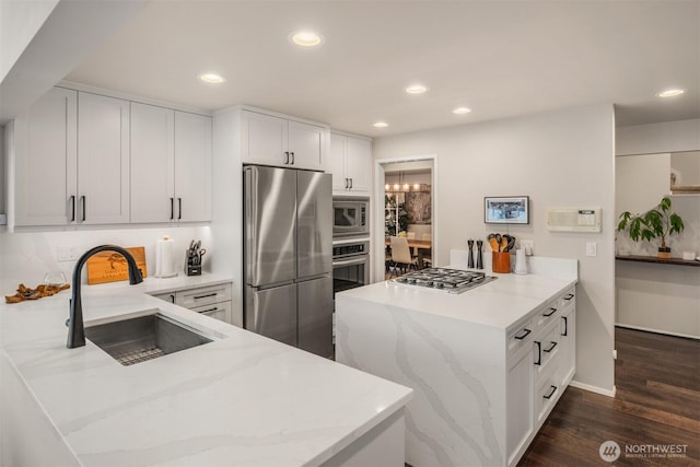 kitchen with a sink, a peninsula, stainless steel appliances, dark wood finished floors, and light stone countertops