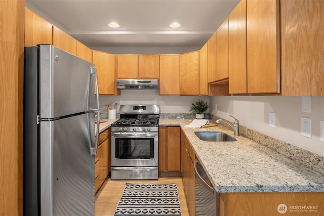 kitchen featuring light stone countertops, under cabinet range hood, a sink, light wood-style floors, and stainless steel appliances