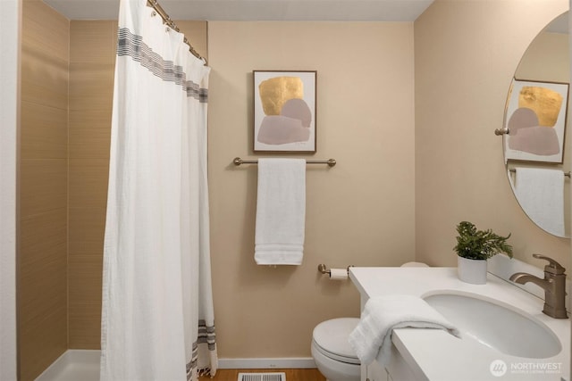 bathroom with a tile shower, baseboards, vanity, and toilet
