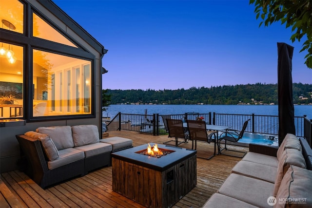 deck at dusk featuring an outdoor living space with a fire pit, a water view, and a view of trees