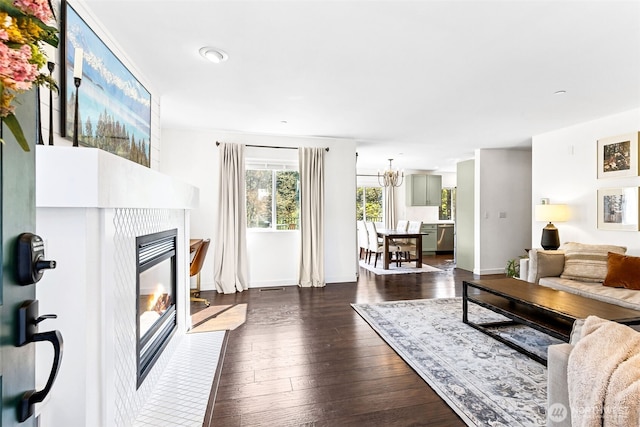 living area with a glass covered fireplace, baseboards, dark wood-style flooring, and a notable chandelier