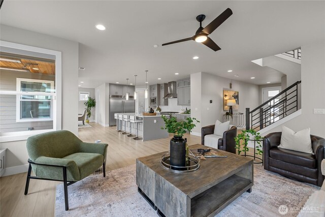 living room featuring baseboards, ceiling fan, light wood-style flooring, and stairway