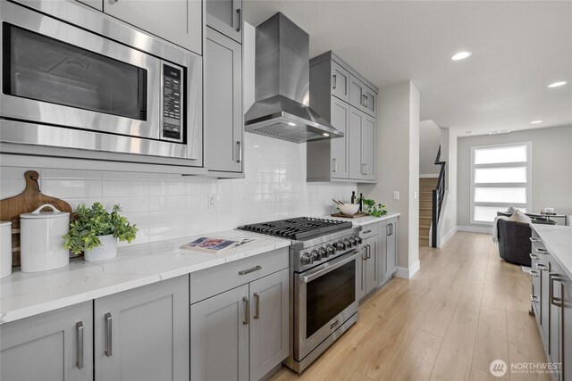 kitchen with baseboards, wall chimney range hood, tasteful backsplash, appliances with stainless steel finishes, and gray cabinetry