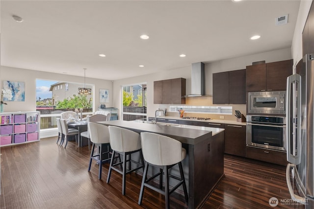 kitchen with a kitchen bar, visible vents, appliances with stainless steel finishes, modern cabinets, and wall chimney exhaust hood