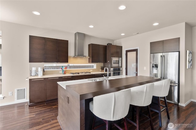 kitchen featuring appliances with stainless steel finishes, a sink, wall chimney exhaust hood, and dark wood-type flooring