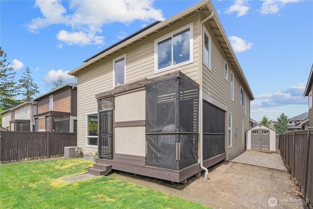 rear view of house with central AC, a shed, a fenced backyard, an outbuilding, and a lawn