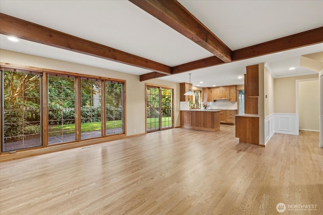 unfurnished living room with beam ceiling, light wood-type flooring, recessed lighting, a wainscoted wall, and a decorative wall