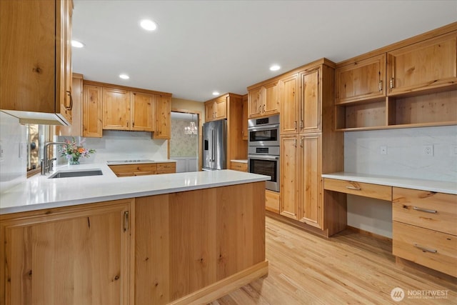 kitchen with appliances with stainless steel finishes, a sink, a peninsula, decorative backsplash, and light wood-type flooring