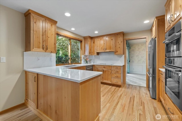 kitchen featuring a sink, stainless steel appliances, light wood-type flooring, a peninsula, and light countertops