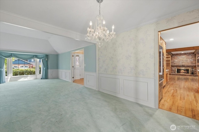 unfurnished dining area with a chandelier, a brick fireplace, a wainscoted wall, carpet flooring, and crown molding