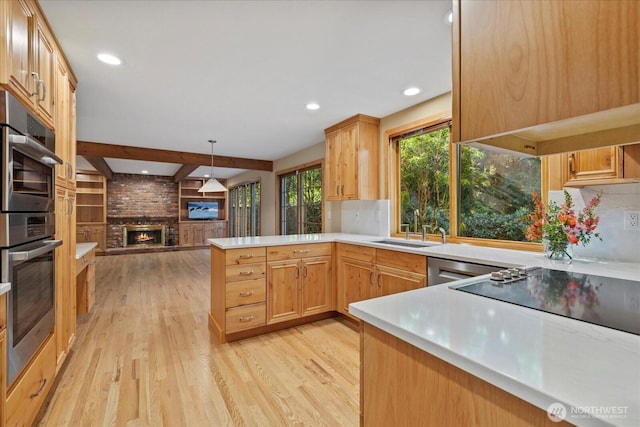 kitchen featuring a sink, a peninsula, a fireplace, light wood-style floors, and tasteful backsplash