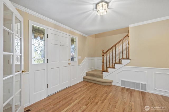 foyer entrance featuring a decorative wall, stairway, a wainscoted wall, wood finished floors, and crown molding