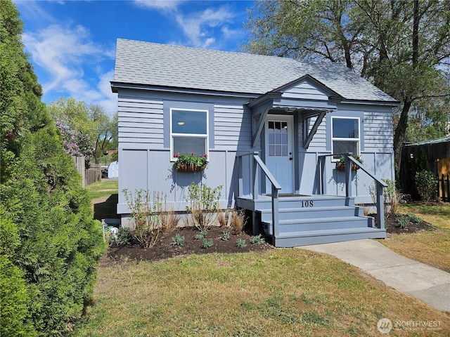 bungalow-style house featuring roof with shingles and a front yard