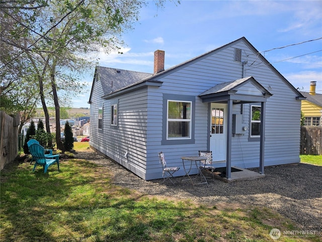 back of house with fence, a chimney, a yard, and roof with shingles