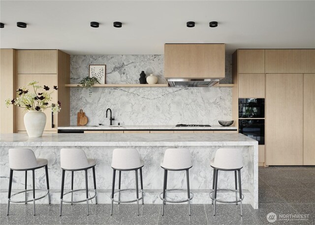 kitchen featuring a kitchen breakfast bar, open shelves, a sink, light stone counters, and ventilation hood