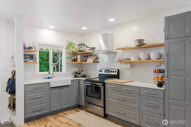 kitchen with open shelves, gray cabinets, wall chimney exhaust hood, stainless steel electric range, and a sink