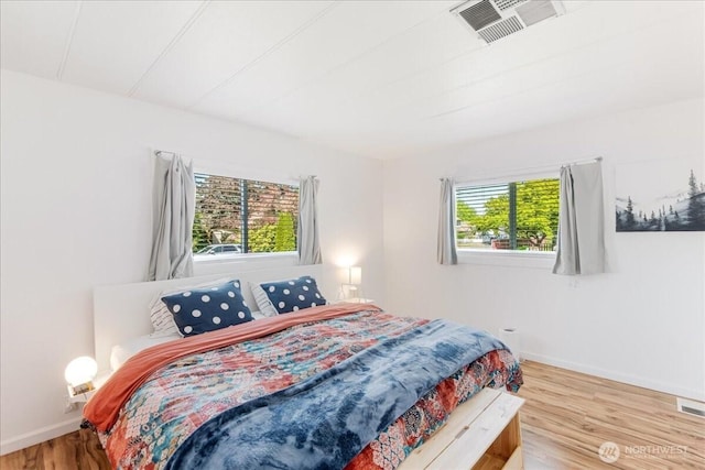 bedroom featuring baseboards, multiple windows, wood finished floors, and visible vents