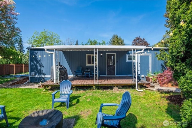 rear view of property featuring fence, a wooden deck, and a lawn