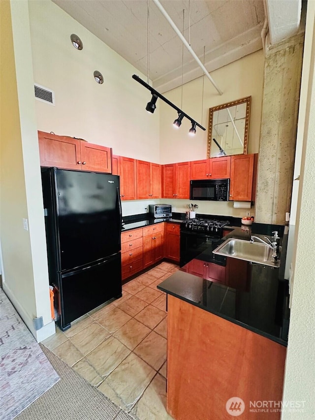 kitchen with a high ceiling, dark countertops, a sink, visible vents, and black appliances