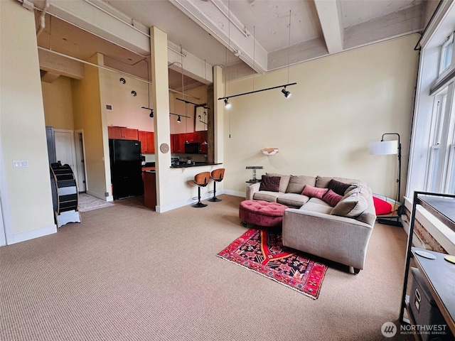 carpeted living area featuring baseboards, a high ceiling, and beam ceiling