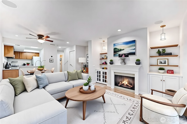 living room with built in features, light wood-style floors, a lit fireplace, recessed lighting, and a ceiling fan