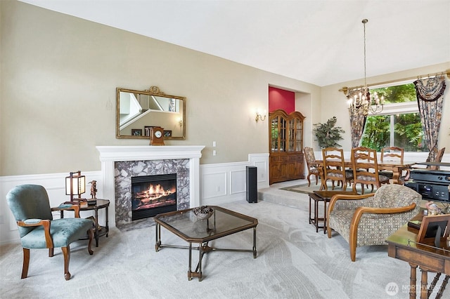 living room with a decorative wall, light colored carpet, a high end fireplace, a wainscoted wall, and a chandelier