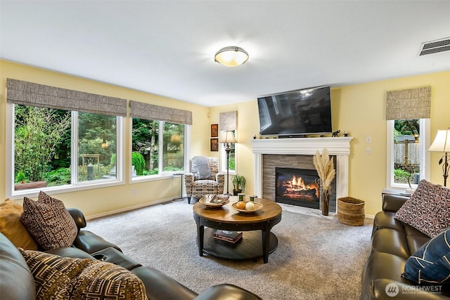 carpeted living room featuring baseboards, visible vents, and a fireplace with flush hearth