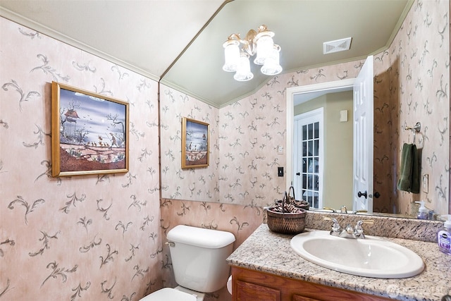 bathroom with visible vents, vanity, toilet, wallpapered walls, and a notable chandelier