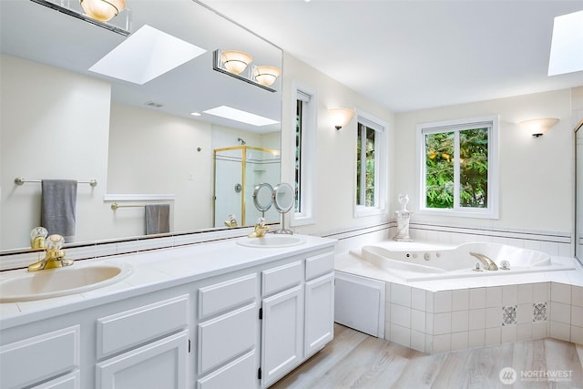 bathroom with a skylight, a jetted tub, a sink, and a stall shower