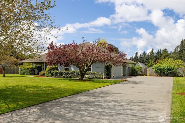 view of property hidden behind natural elements featuring fence, driveway, a front yard, and a garage