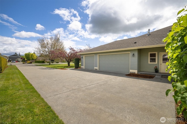 view of side of property with concrete driveway, an attached garage, roof with shingles, and a yard