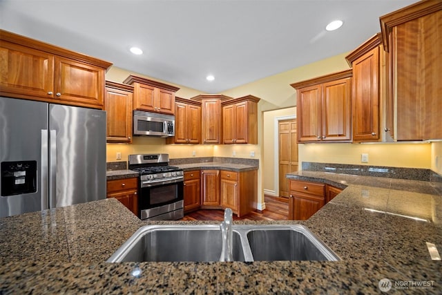 kitchen with brown cabinetry, a sink, dark wood-style floors, and stainless steel appliances