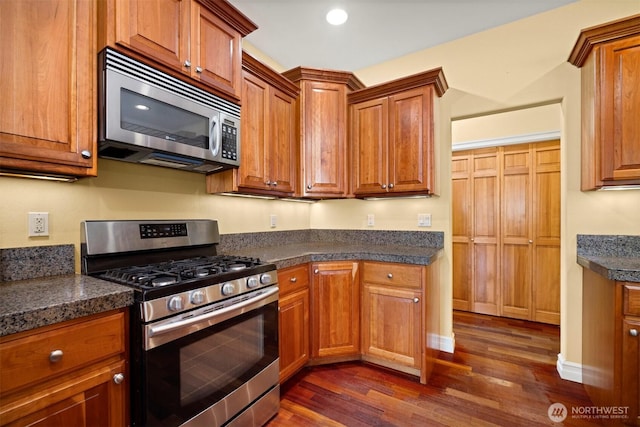 kitchen with dark countertops, brown cabinets, stainless steel appliances, and dark wood-style flooring
