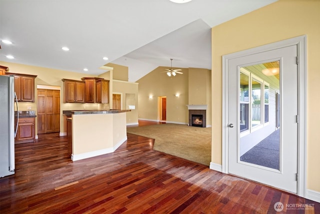 kitchen with brown cabinetry, freestanding refrigerator, open floor plan, ceiling fan, and dark wood-type flooring