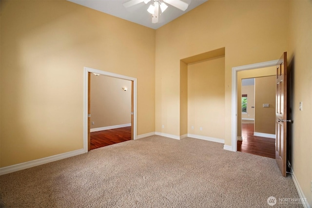 empty room with carpet flooring, ceiling fan, baseboards, and a towering ceiling