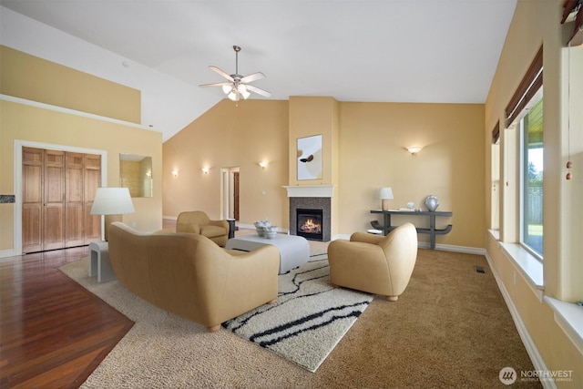 living area featuring baseboards, a ceiling fan, a glass covered fireplace, and high vaulted ceiling