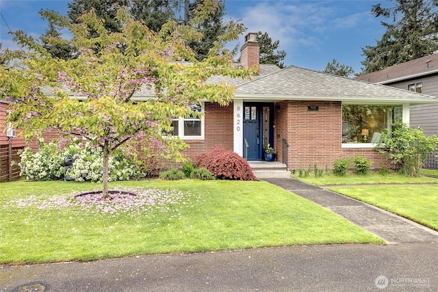 ranch-style house with brick siding, a shingled roof, a front lawn, and a chimney