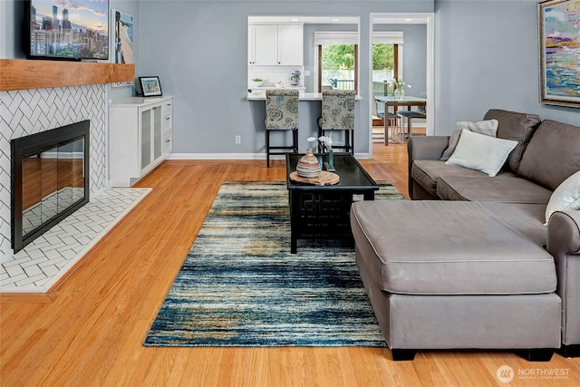 living area with baseboards, a fireplace with flush hearth, and light wood finished floors