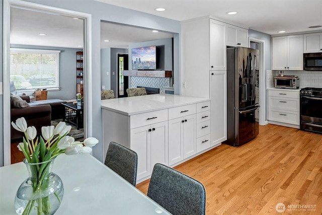 kitchen with black fridge with ice dispenser, light wood-type flooring, gas range oven, stainless steel microwave, and tasteful backsplash