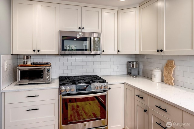 kitchen featuring decorative backsplash, light stone countertops, stainless steel appliances, and white cabinetry